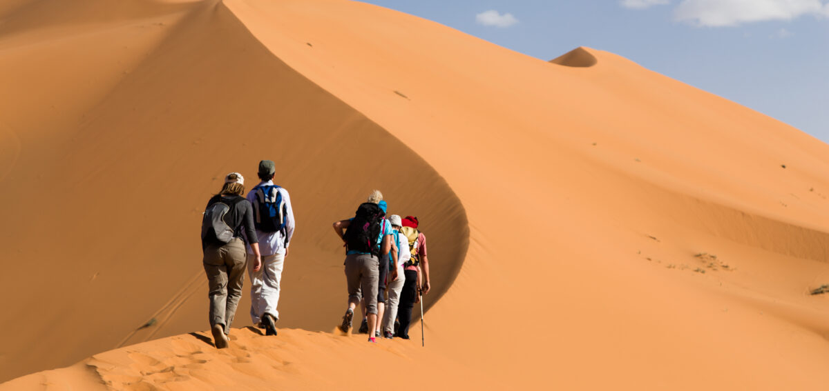 Tourists climbing the golden sand dunes of Merzouga Sahara Desert in Morocco