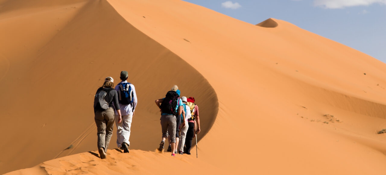Tourists climbing the golden sand dunes of Merzouga Sahara Desert in Morocco