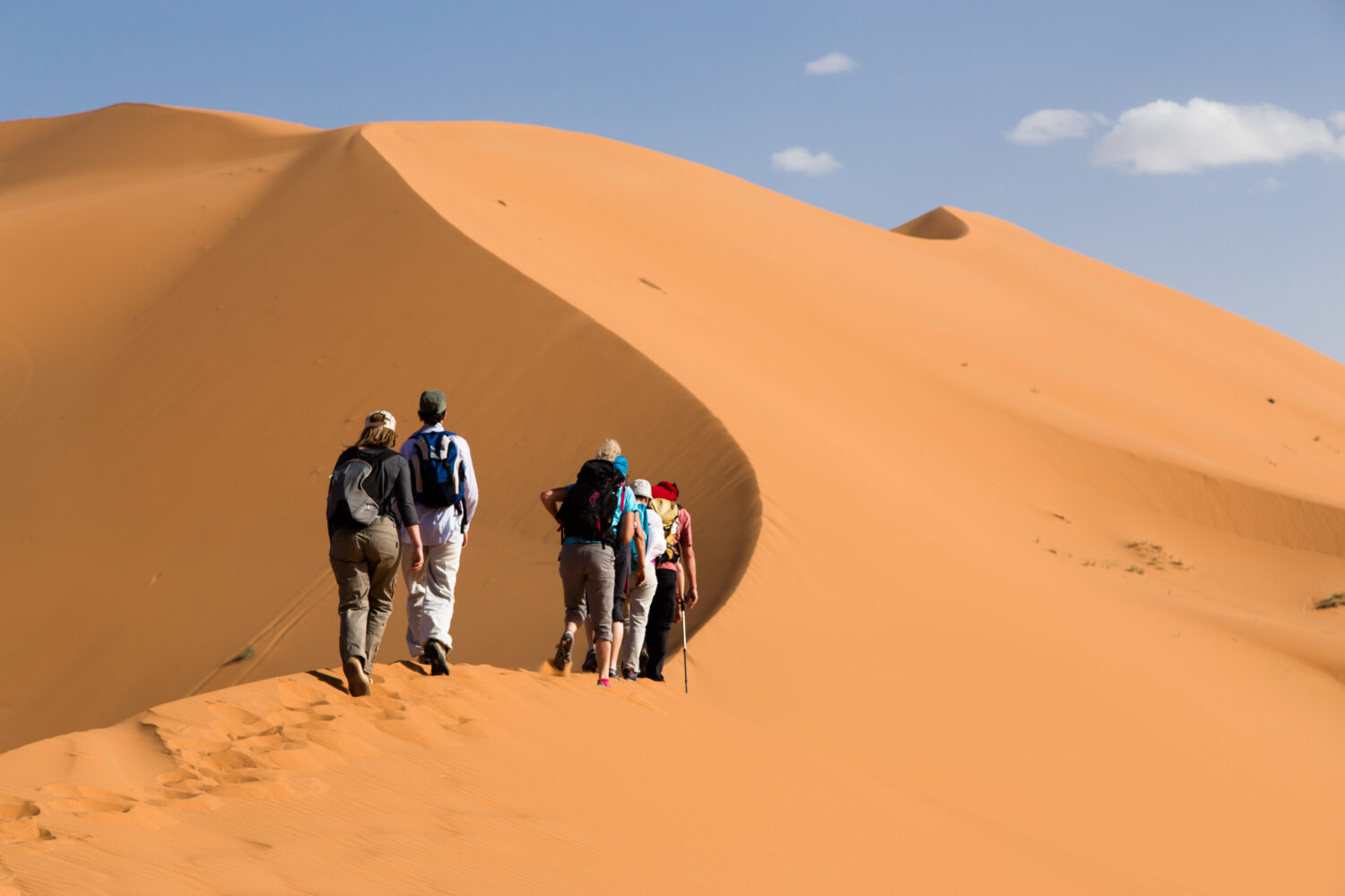 Tourists climbing the golden sand dunes of Merzouga Sahara Desert in Morocco