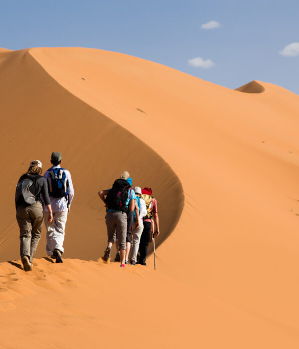 Tourists climbing the golden sand dunes of Merzouga Sahara Desert in Morocco
