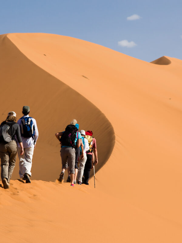 Tourists climbing the golden sand dunes of Merzouga Sahara Desert in Morocco