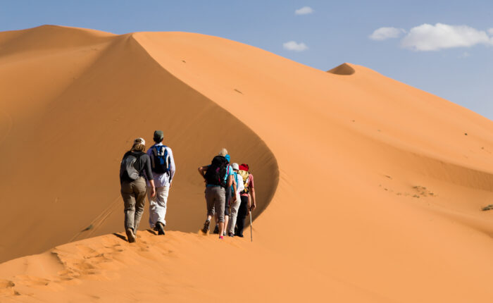 Tourists climbing the golden sand dunes of Merzouga Sahara Desert in Morocco