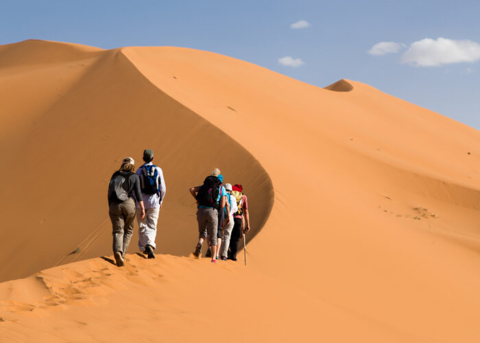Tourists climbing the golden sand dunes of Merzouga Sahara Desert in Morocco