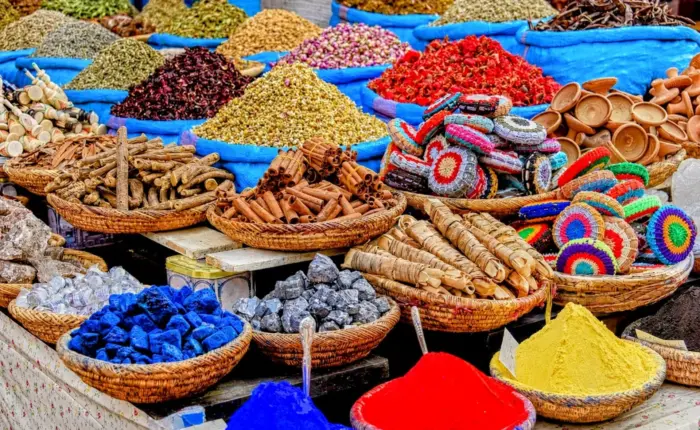 Colorful display of Moroccan spices, herbs, natural dyes, rose petals, soaps, and traditional products arranged in baskets at a local souk.