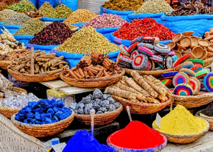 Colorful display of Moroccan spices, herbs, natural dyes, rose petals, soaps, and traditional products arranged in baskets at a local souk.