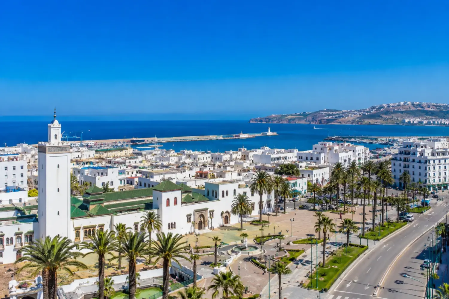 Panoramic view of Tangier, Morocco, featuring the historic Kasbah, palm-lined avenues, whitewashed buildings, and the Mediterranean coastline under a clear blue sky visited on 9 Day Sahara Desert Tour from Tangier to Marrakech