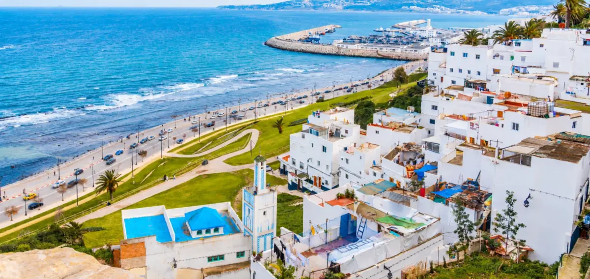 Panoramic view of Tangier coastline with white buildings, blue sea, palm trees, and the city harbor under a clear sky.