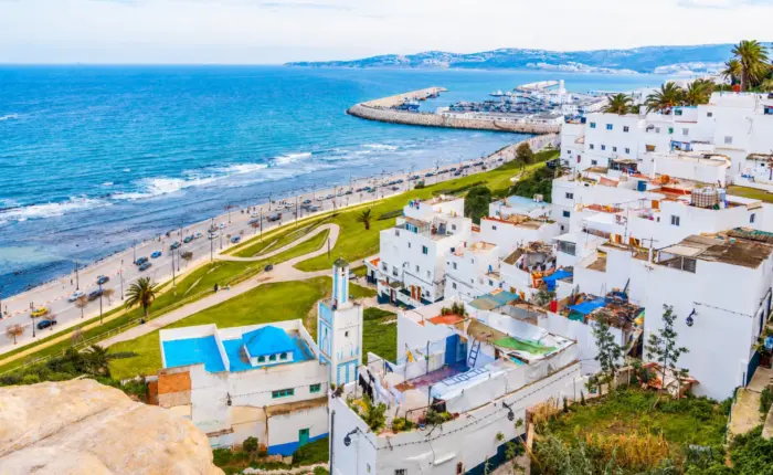 Panoramic view of Tangier coastline with white buildings, blue sea, palm trees, and the city harbor under a clear sky.