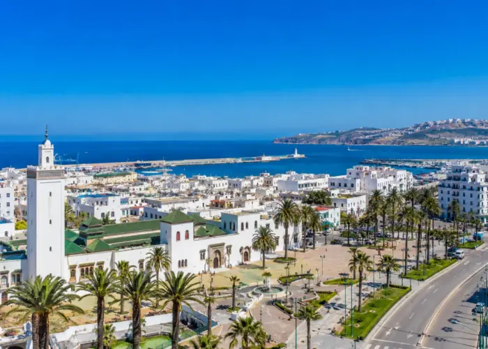 Panoramic view of Tangier, Morocco, featuring the historic Kasbah, palm-lined avenues, whitewashed buildings, and the Mediterranean coastline under a clear blue sky visited on 9 Day Sahara Desert Tour from Tangier to Marrakech