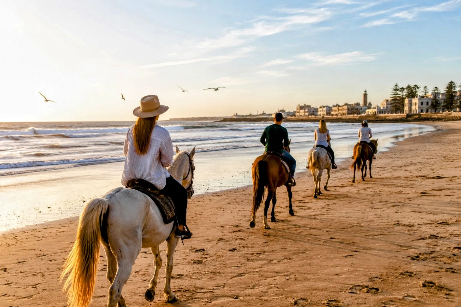 Best Things To Do in Essaouira Travelers riding horses along the beach during sunset on Morocco’s Atlantic Coast