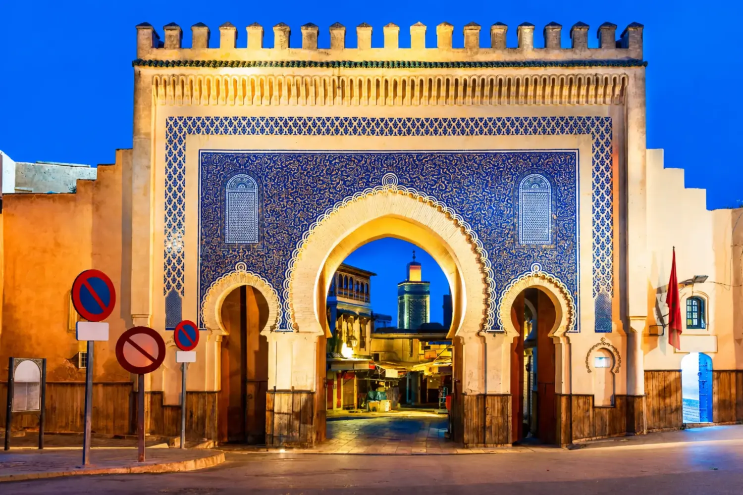 Illuminated Bab Bou Jeloud gate in Fes featuring intricate blue zellige tilework and traditional Moroccan architecture at night during 3 Day Tour from Fes to Marrakech via Chefchaouen