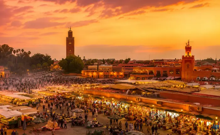 Marrakech Jemaa el-Fna Square at sunset with the Koutoubia Mosque, colorful market stalls, and vibrant city atmosphere.