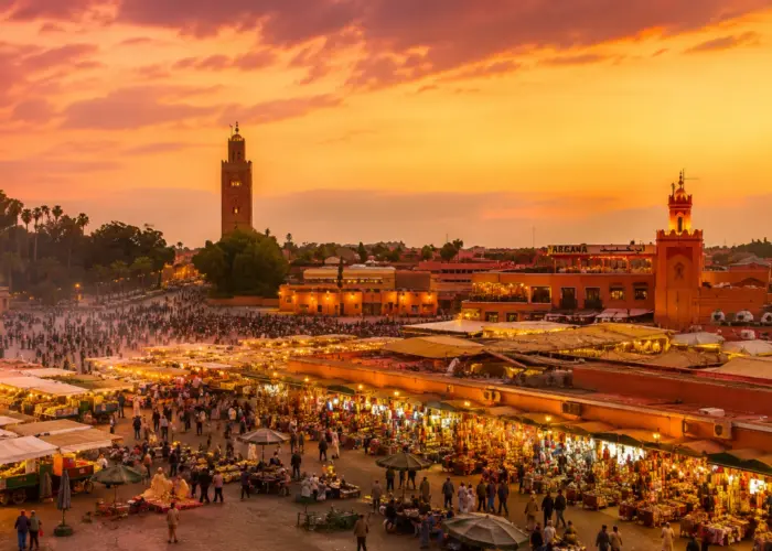 Marrakech Jemaa el-Fna Square at sunset with the Koutoubia Mosque, colorful market stalls, and vibrant city atmosphere.