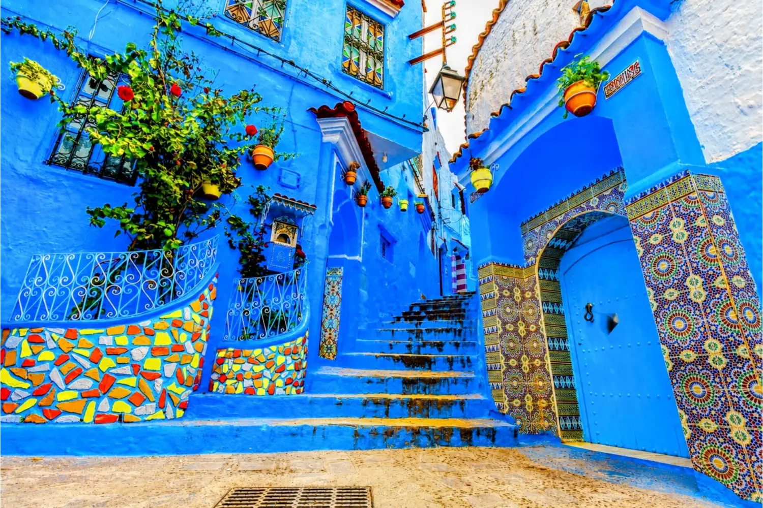 Colorful blue alleyway in Chefchaouen, Morocco, featuring traditional houses, tiled archways, and vibrant flower pots during 3 Day Tour from Fes to Marrakech via Chefchaouen