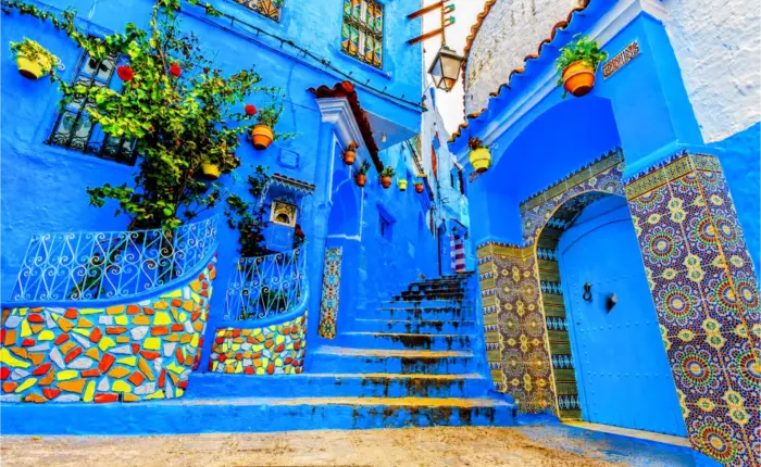Colorful blue alleyway in Chefchaouen, Morocco, featuring traditional houses, tiled archways, and vibrant flower pots during 7 Day Tour Sahara and Chefchaouen from Casablanca