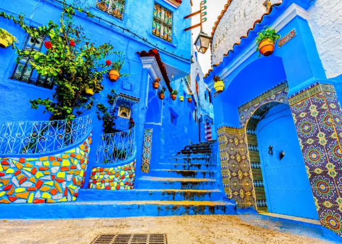 Colorful blue alleyway in Chefchaouen, Morocco, featuring traditional houses, tiled archways, and vibrant flower pots.
