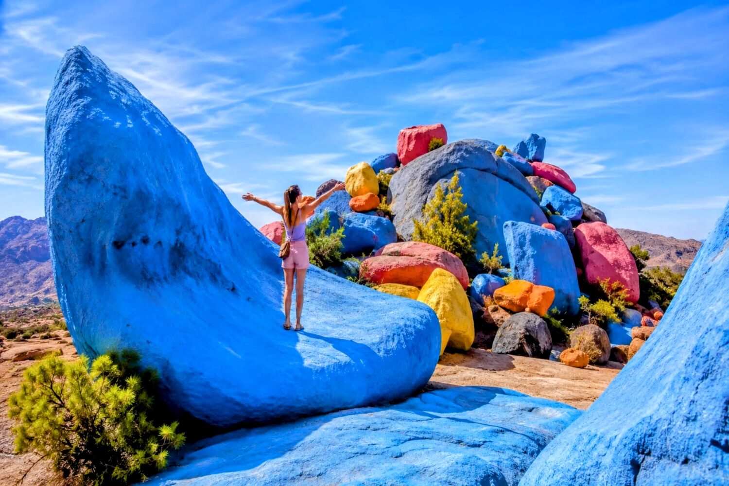 Tourist enjoying the colorful painted rocks near Tafraoute in Morocco's Anti-Atlas Mountains visited during the 30 Day Morocco Explorer Tour from Casablanca.